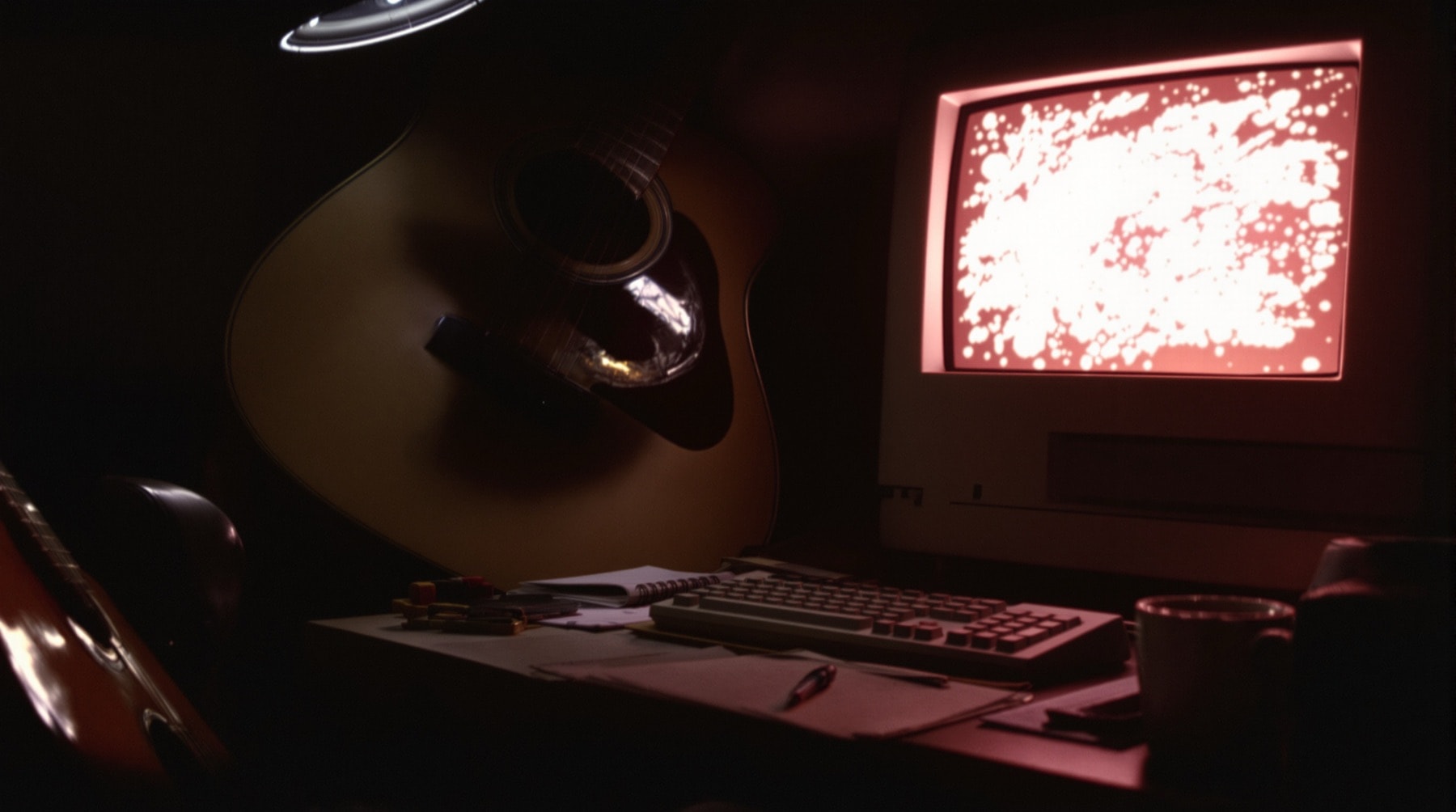A late-1990s desk with a glowing monitor and an acoustic guitar leaning beside it