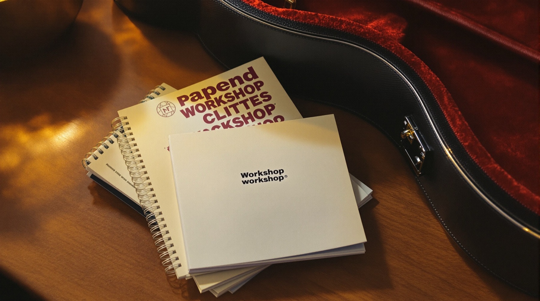 A stack of workshop brochures and a notebook on a desk beside a guitar case